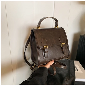 Detail of dark brown vintage faux leather backpack featuring golden buckles and top handle