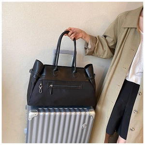 Close-up of black nylon tote bag with dual handles placed on silver metal luggage