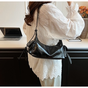 Close-up of black glossy PU leather shoulder bag with side pocket on a female model
