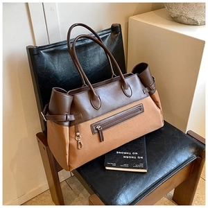 Detail of a two-tone canvas and brown leather tote bag with pocket and metal hooks