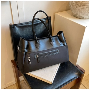 Detail of black tote bag featuring mixed textures, front zipper pocket, and metal buckles