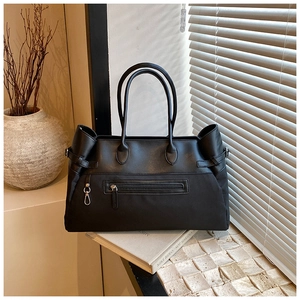 Detail of black tote bag with front zipper and side buckle straps in lifestyle setting