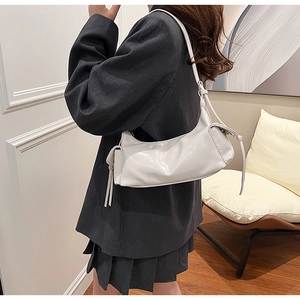Side view of white glossy leather shoulder bag with tassels styled on female model