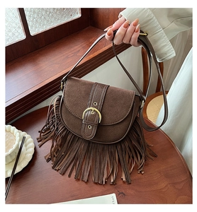 Detailed close-up of dark brown suede shoulder bag featuring fringe and metal buckle strap