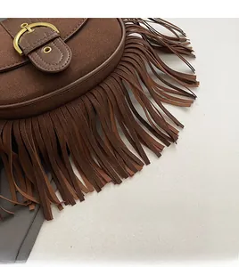 Detail of brown suede saddle bag featuring long tassels and a golden horseshoe buckle
