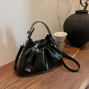 Sac nuage plissé noir brillant avec chaîne sur une table en bois rustique
