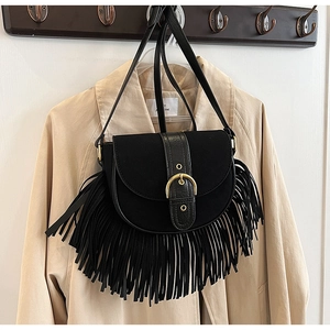 Detail of a black suede tassel saddle bag with a large gold buckle against a beige coat