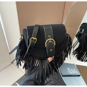 Detail of black suede saddle bag with long tassels and gold metal buckle on a desk