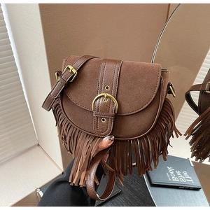 Detailed macro view of brown suede saddle bag featuring long fringe and gold buckle