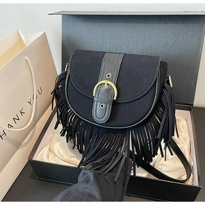 Detail view of black suede saddle bag with fringe and gold ring in a luxury gift box