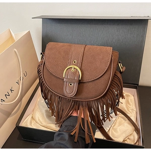 Close-up of brown suede saddle bag with tassels and gold buckle in a gift box