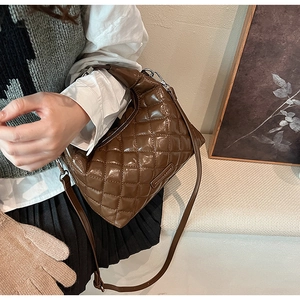 Detail view of dark brown quilted shoulder bag with glossy finish and metal logo plaque