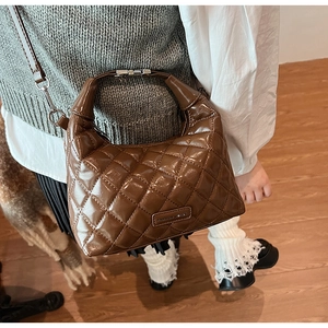 Detail of quilted brown leather bag with metallic logo plate and adjustable strap