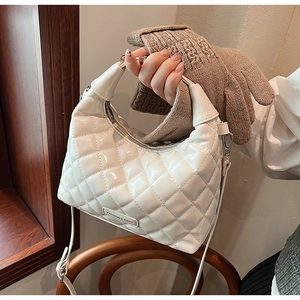 Detail view of white quilted faux leather handbag with silver logo plate on wooden surface