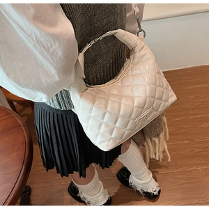 Close-up of white quilted handbag with metallic ring handle and a long shoulder strap