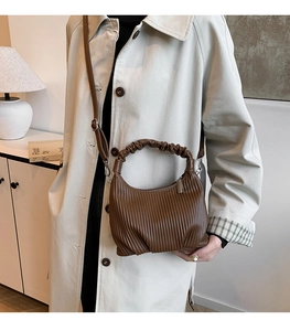 Close-up of brown pleated PU leather handbag with ruched handle and silver zipper detail