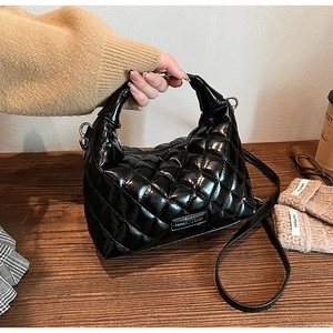 Close-up of black quilted leather crescent bag with metal tag on a wooden surface