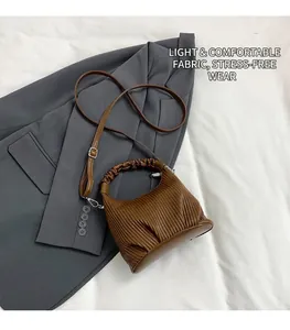 Macro detail of brown pleated leather handbag with adjustable strap on a gray blazer