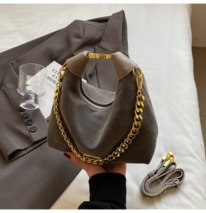 Détail du sac en daim gris avec poignée dorée incurvée et chaîne métallique épaisse
