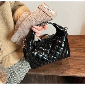 Detail of black patent leather quilted bag with silver metal handle and shoulder strap