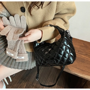 Detail of a black quilted patent leather hobo bag with khaki knitted gloves on a wooden surface