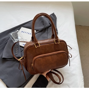 Close-up of vintage brown PU leather bag with tassel detail and bronze hardware on white bed