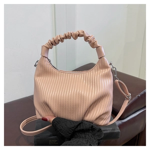 Detail of pink ruched cloud handle handbag with textured crescent shape on dark books