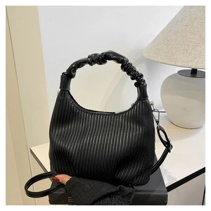 Detail of black pleated crossbody bag with a scrunchie top handle and adjustable strap