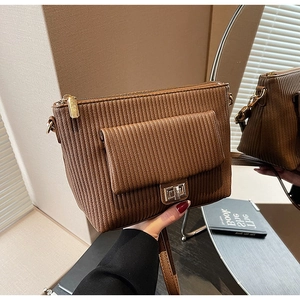Detail of dark brown ribbed crossbody bag featuring a golden twist lock and vertical texture