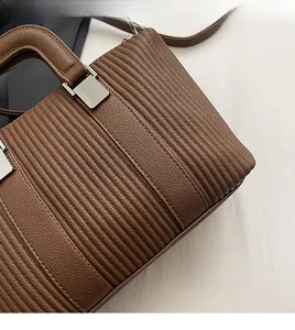 Detail of brown litchi pattern leather bag with horizontal pleated stitching and silver buckle