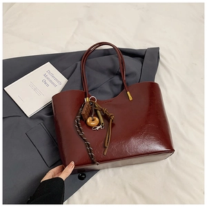 Dettaglio della borsa tote rosso scuro con trama in pelle lucida e ciondoli trendy