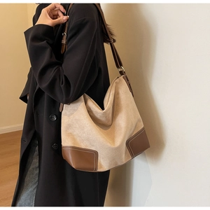 Close-up of beige suede hobo bag with brown leather corners and white contrast stitching