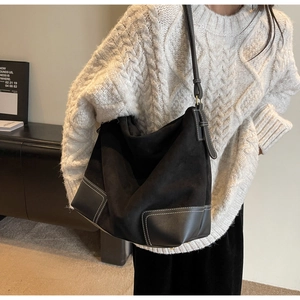 Close-up of black suede tote bag with contrast white stitching and leather strap detail