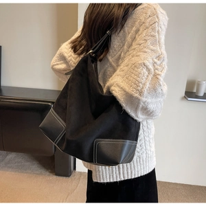 Detail view of large black suede tote bag with contrast stitching on white sweater