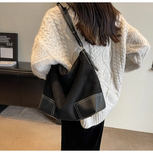 Detailed view of black suede shoulder bag with contrast white stitching and leather patchwork