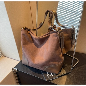 Detail of dark brown suede tote featuring contrast white stitching and gold hardware accents
