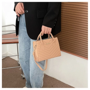 Model holding a khaki V-quilted faux leather handbag with adjustable shoulder strap