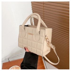 Detail of beige quilted handbag with metal logo on dark wood background