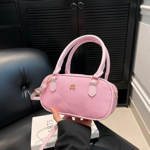 Pink cylinder handbag with gold logo and adjustable strap in a modern lifestyle setting