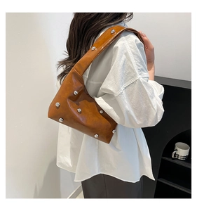 Detail van caramelbruine schoudertas met zilveren klinknagels gedragen door een model