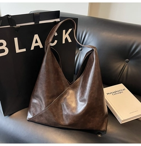Close-up of minimalist dark brown leather tote bag with unique triangular shape and wide strap