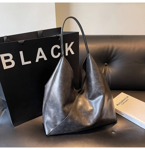 Detail of dark grey tote bag with geometric stitching on a luxury leather sofa