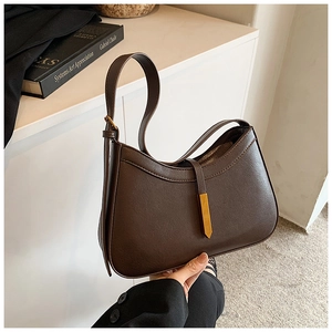 Détail d'un sac sous le bras en cuir marron foncé avec boucle dorée et bandoulière