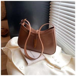 Gros plan du sac hobo en cuir marron avec boucle en métal doré sur un blazer blanc