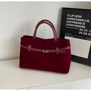 Close-up of deep red velvet tote bag with leather strap detail and metal buckle