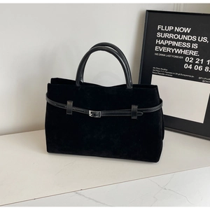 Detail of black suede handbag with leather buckle strap on marble surface