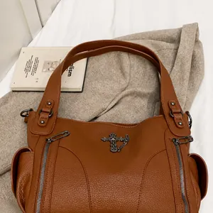 Close-up of brown textured leather tote bag with gothic cross and side zipper details