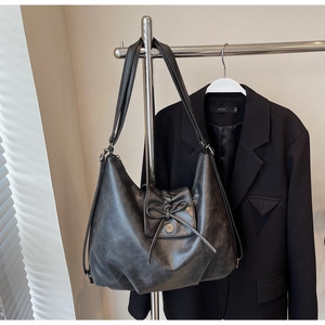 Detail of black hobo bag with a decorative bow and metallic ring on faux leather