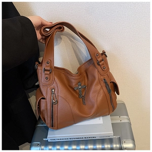 Brown textured leather tote with gothic cross charm and zippers on a silver suitcase