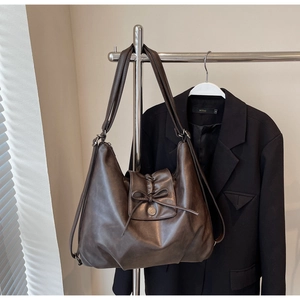 Detailed view of brown leather tote bag with decorative bow and vintage metal buckle detail